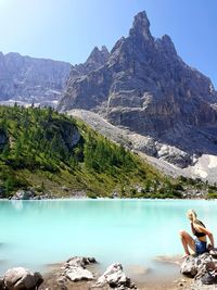 Woman sitting on rock while looking at scenic lake and mountains