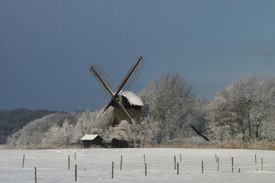 Traditional windmill on field against clear sky during winter