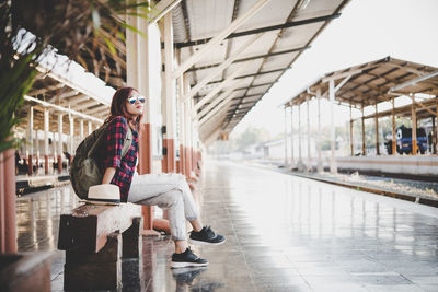 Side view full length of young woman on seat at railroad station platform
