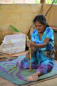 Mature woman holding firewood while sitting on carpet 