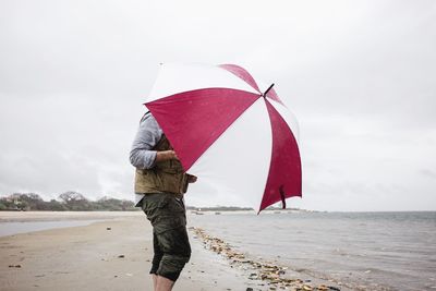 Man with umbrella standing at beach against sky