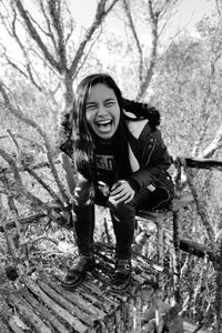 Portrait of young woman laughing while sitting against trees