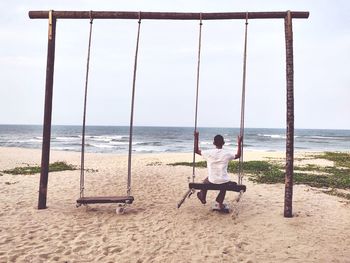 Rear view of woman on swing at beach against sky