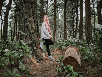 Full length of woman standing on tree trunk in forest