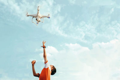 Low angle view of boy reaching for drone flying against sky