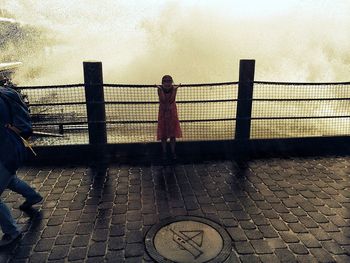 Man standing on railing against sky