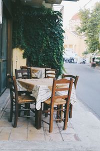 Empty chairs and tables at sidewalk cafe by buildings