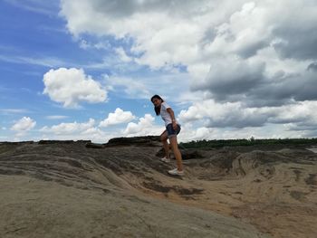 Side view of young man jumping on land against sky