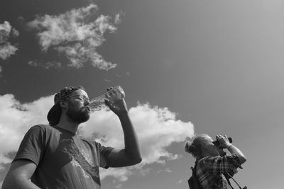 Man drinking water while woman looking through binoculars against sky