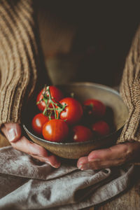 Cropped hands of woman holding bowl with cherry tomatoes on table