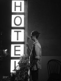 Side view of young man smoking by illuminated sign