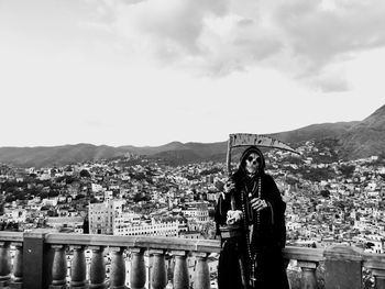 Man standing on railing in city against sky