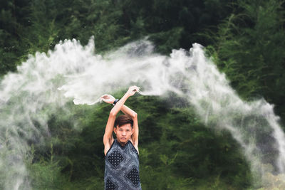 Portrait of man throwing sand mid-air against plants