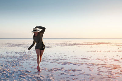 A young caucasian attractive slender woman is walking along a pink sunlit lake balancing on her toes