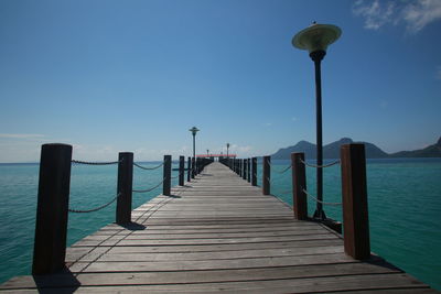 Wooden pier on sea against clear blue sky