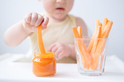 Midsection of baby girl sitting with carrots at home