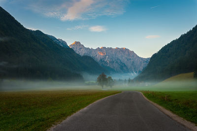 Empty road on field leading towards mountains against sky during foggy weather