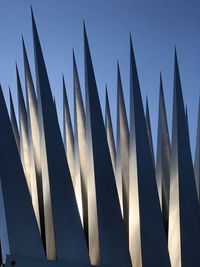 Low angle view of spiked metallic art structure against blue sky