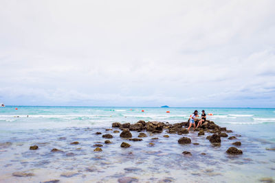 Women sitting on rocks at beach against sky