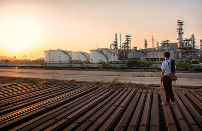 Full length of man standing by factory against sky during sunset