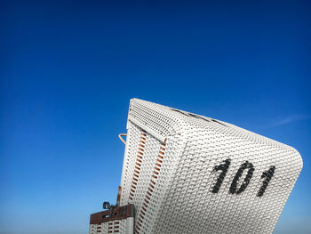 Traditional north german white beach chair with black number 101 at north sea beach against blue sky