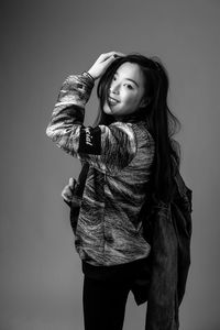 Young woman looking away while standing against gray background