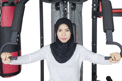Portrait of confident young woman wearing hijab exercising against white background