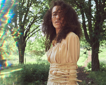 Portrait of woman tied with rope while standing against trees