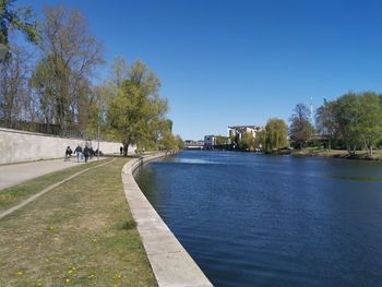 People on footpath by river against clear blue sky