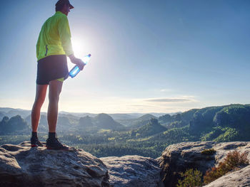 Man standing on rock looking at mountains against sky
