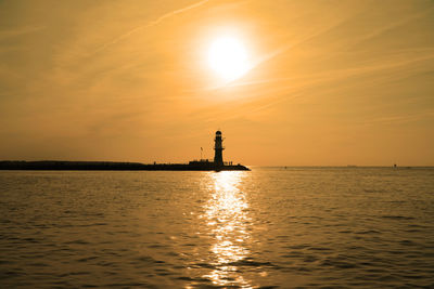 Silhouette lighthouse by sea against sky during sunset