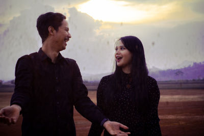 Young couple on field standing against sky