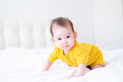 Healthy asian baby girl 5 months in yellow bodysuit on bed on white bedding