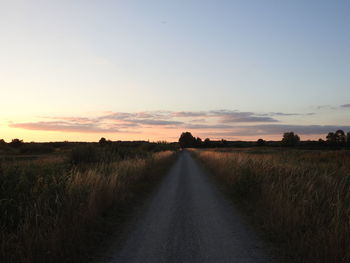 Road amidst field against sky during sunset