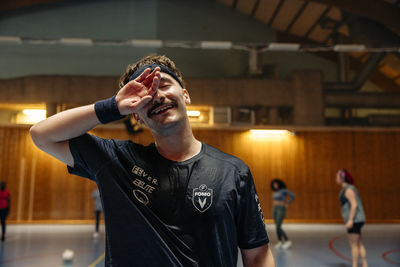 Smiling male athlete rubbing eye at sports court