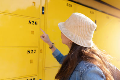 Side view of woman wearing hat while pointing at closed yellow lockers