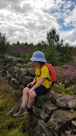 Full length of girl sitting on rock against sky