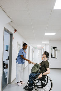 Smiling female healthcare worker doing handshake with boy sitting on wheelchair at hospital