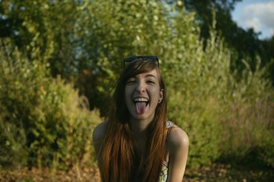 Portrait of woman sticking out tongue against trees