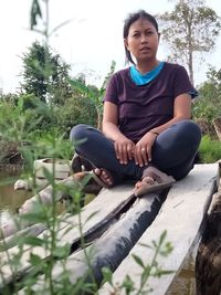 Young woman sitting by plants against trees