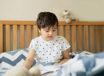 Cute boy sitting on bed at home