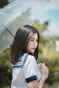 Young woman with umbrella standing against sky