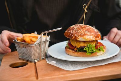 Midsection of man eating fresh burger and french fries at restaurant