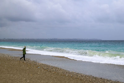 Rear view of woman walking at beach against sky