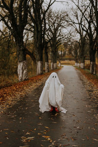 Little ghost standing on the road in red boots. autumn halloween