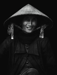 Portrait of senior woman wearing asian style conical hat against black background