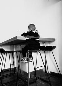 Rear view of boy sitting on table at home