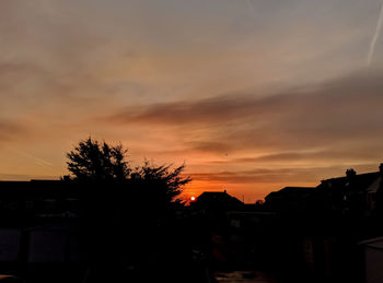 Silhouette trees and buildings against sky at sunset