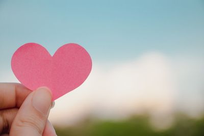 Close-up of hand holding heart shape against sky