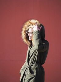 Side view of happy young woman wearing fur coat against red wall